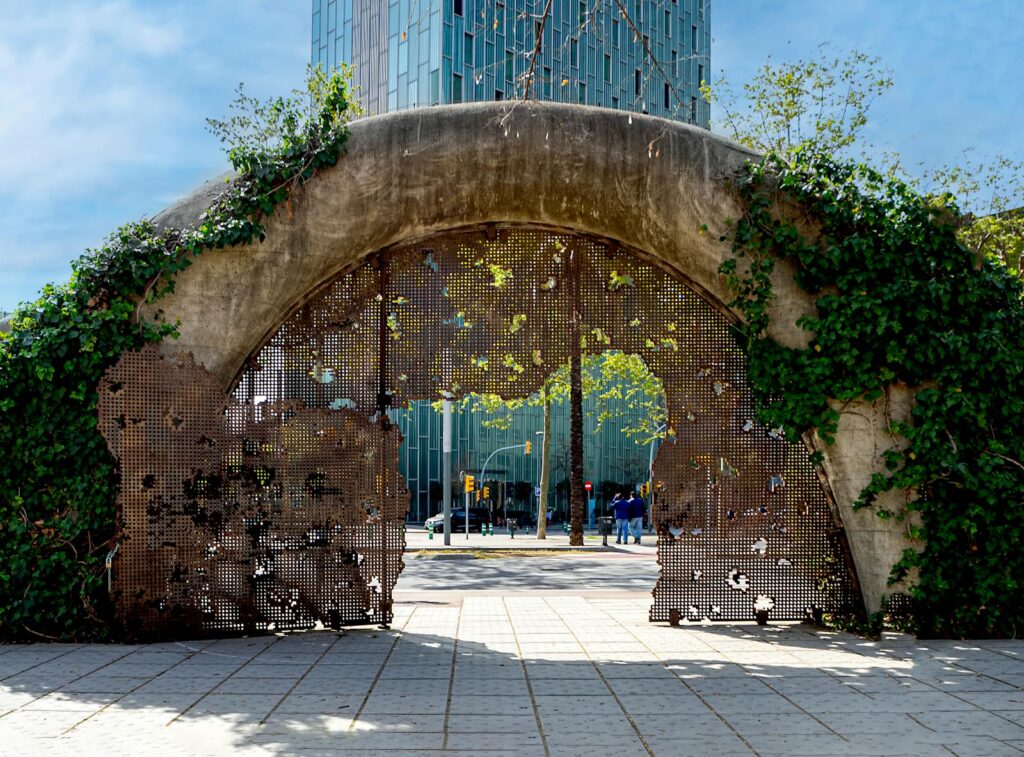 A unique archway entrance with greenery near modern buildings in Barcelona.